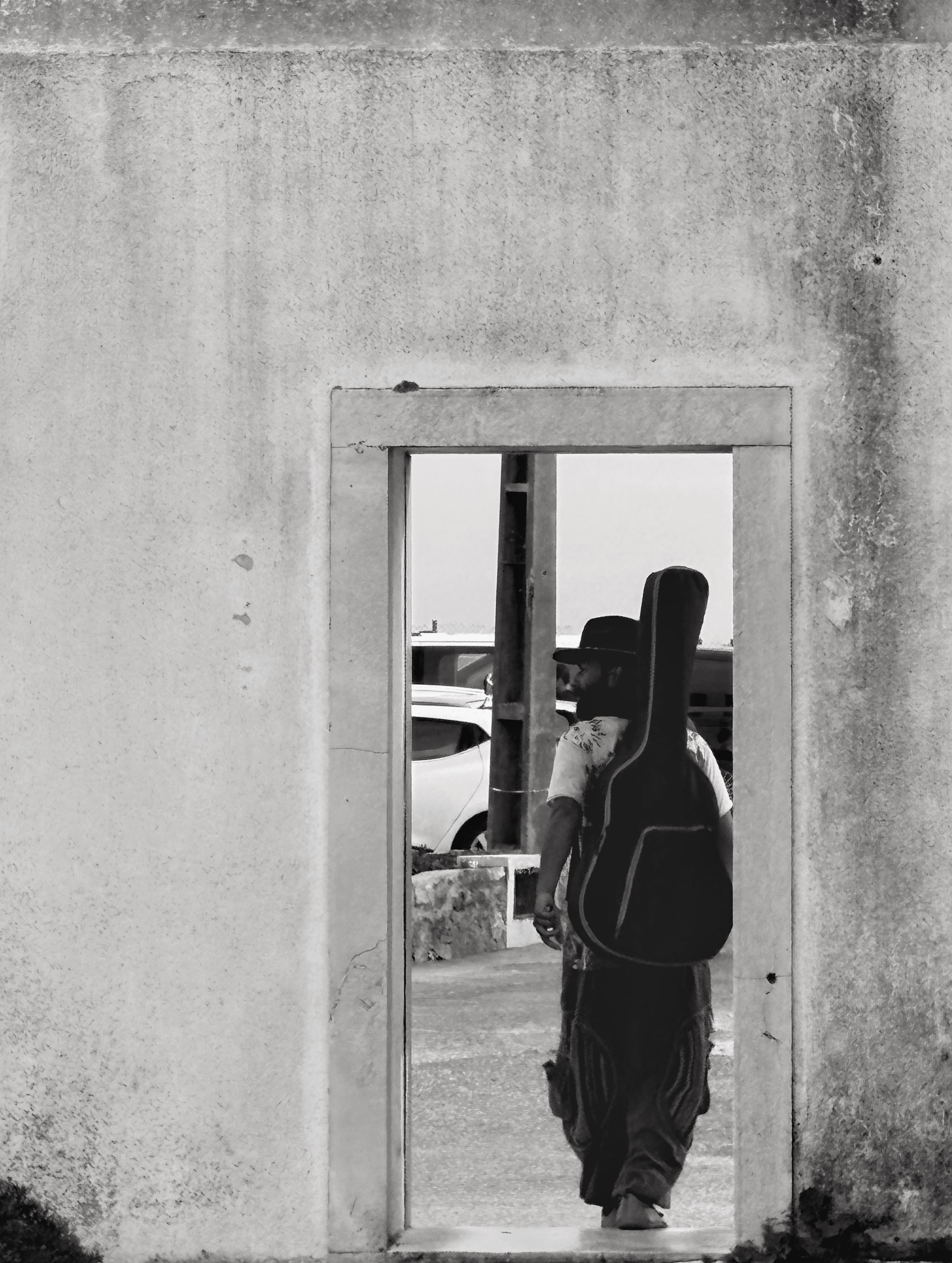 Bibash Upreti walking through a doorway, guitar on his back, hat on